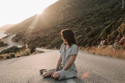 A woman sitting on a coastal road in Antalya during sunset, offering a serene landscape view.