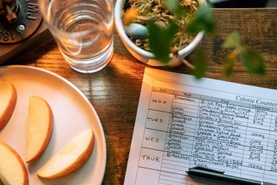 Top view of apple slices, water, and a calorie counter sheet on a wooden table promoting a healthy lifestyle.